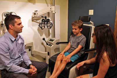 Optometrist Dr. Taylor Kneip examing a boy's eyes and talking with his mom