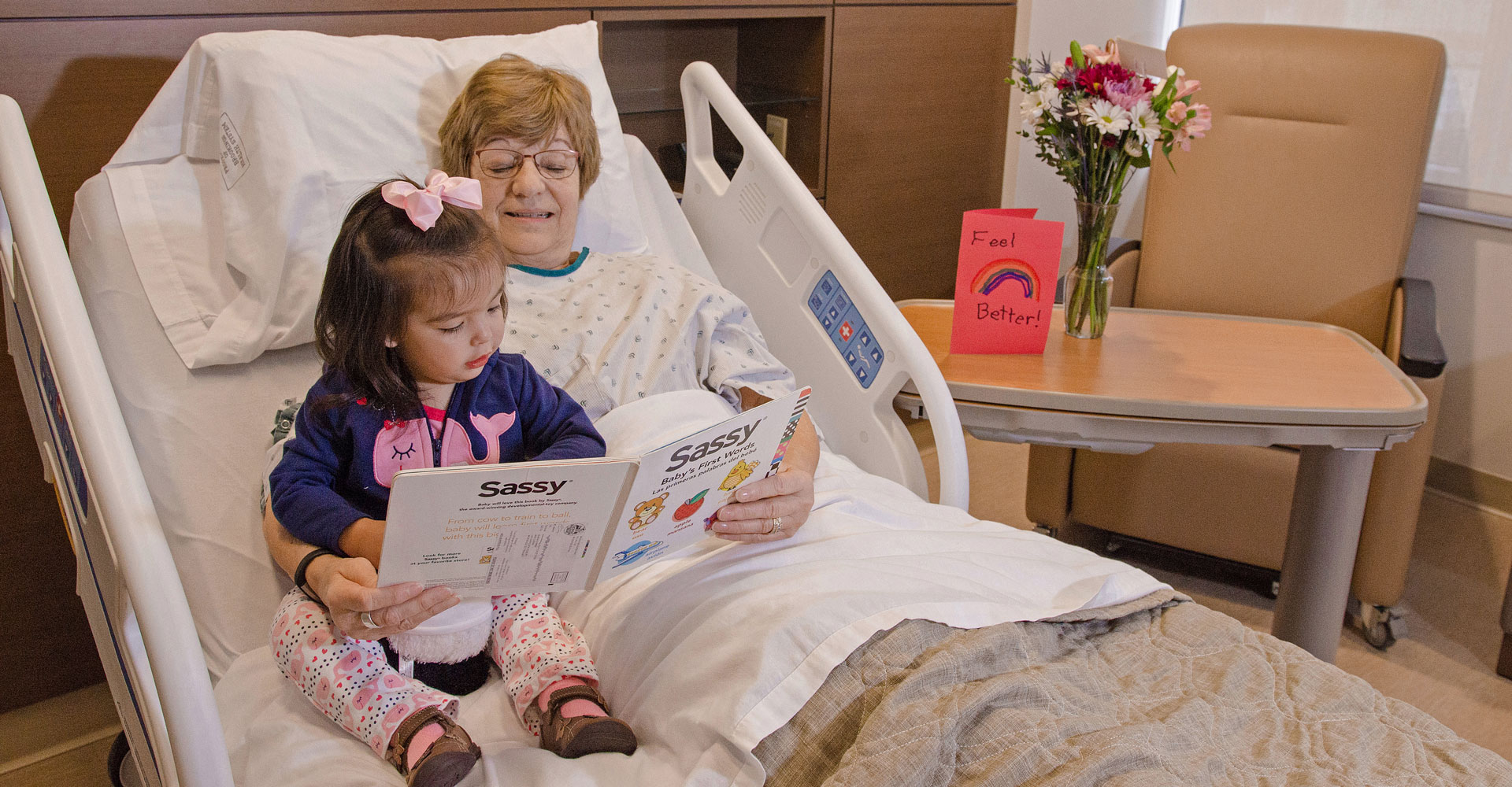 Grandma reading to little granddaughter while she visits grandma in the hospital