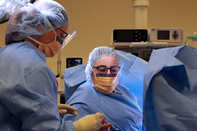 Surgical tech handing Gynecologist Dr. Kirstin Sholes a tool during a surgical procedure