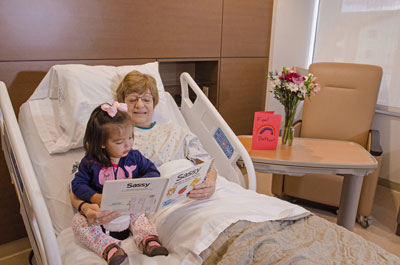 Female patient reading to visiting granddaughter while sitting in bed